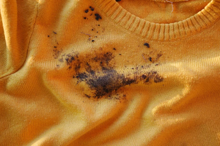 Orange knit sweater with dark, muddy stains and scattered debris across the front near the neckline.