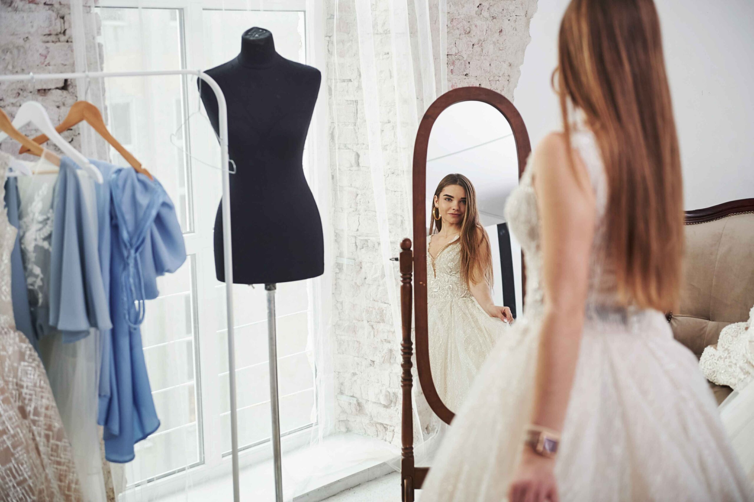Woman trying on an elegant gown in front of a mirror, showing tailoring details that explain What Is the Difference Between a Dress and a Frock in real fashion use.